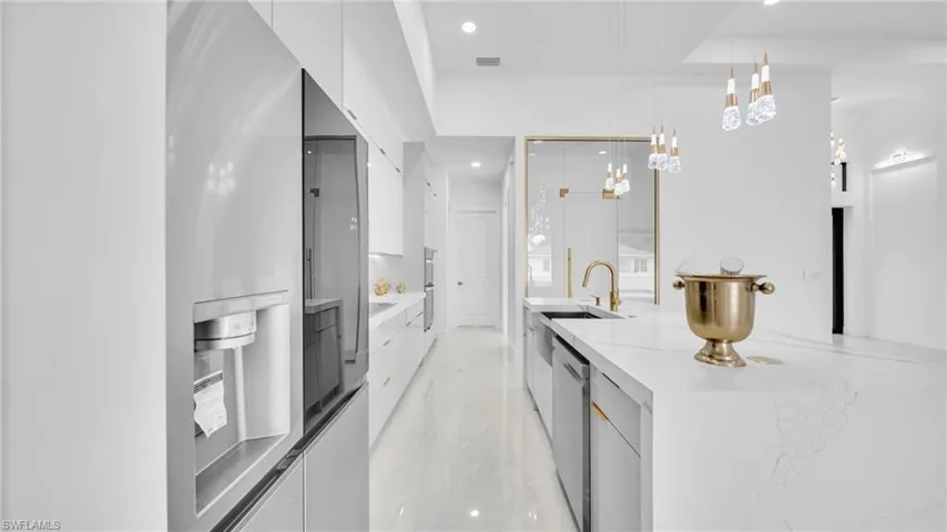 Kitchen with modern cabinets, white cabinets, appliances with stainless steel finishes, decorative light fixtures, and recessed lighting