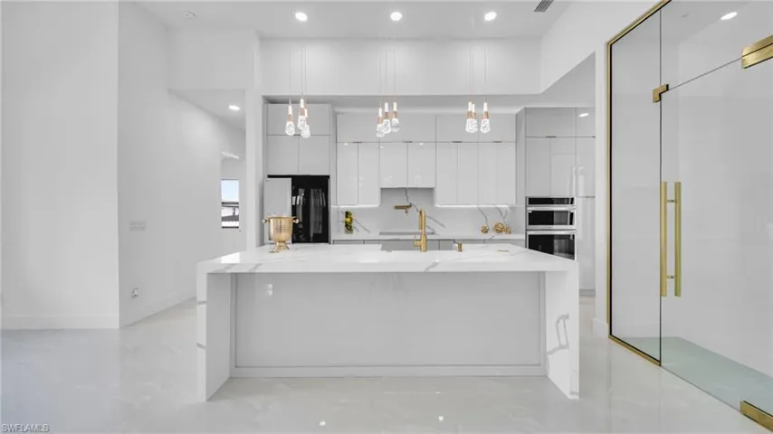 Kitchen featuring modern cabinets, white cabinetry, recessed lighting, freestanding refrigerator, and a large island with sink