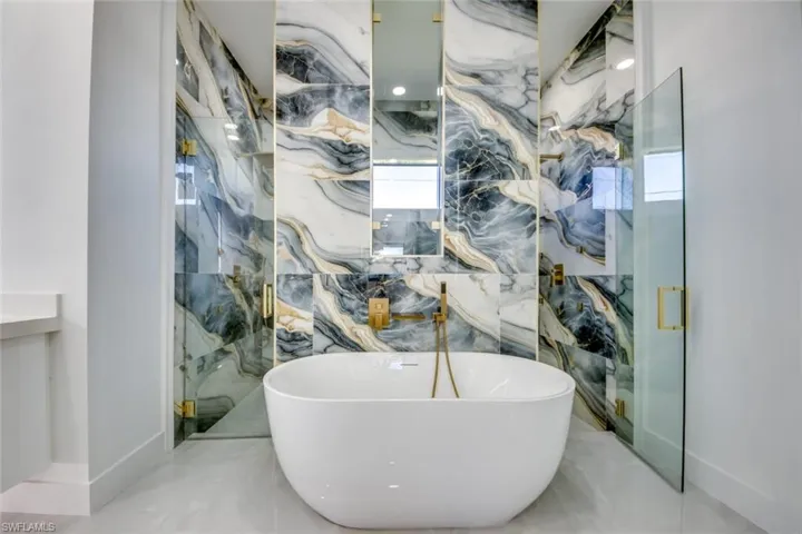 Bathroom with a freestanding bath, a marble finish shower, and marble tiled floors