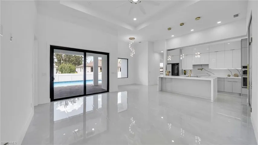 Unfurnished living room featuring a towering ceiling, a raised ceiling, recessed lighting, a chandelier, and ceiling fan