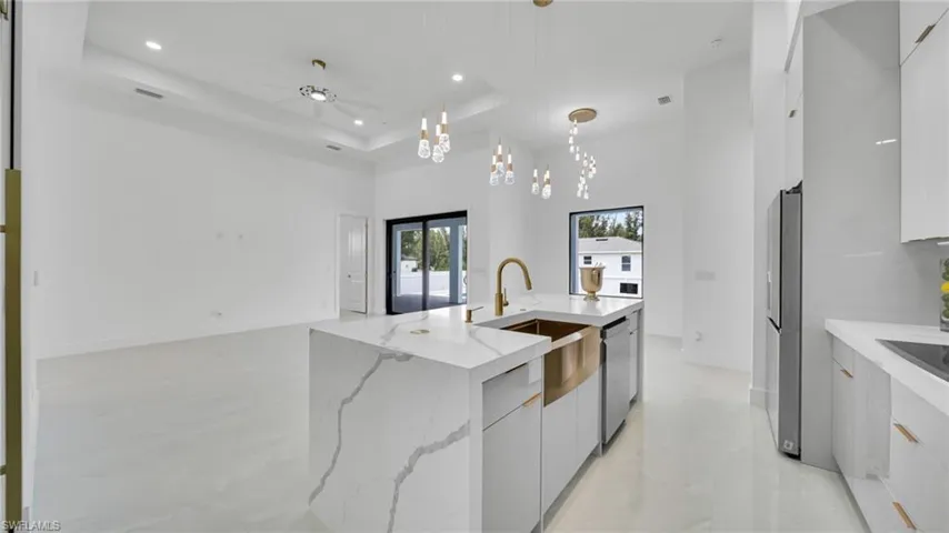 Kitchen featuring modern cabinets, a raised ceiling, a spacious island, decorative light fixtures, and ceiling fan