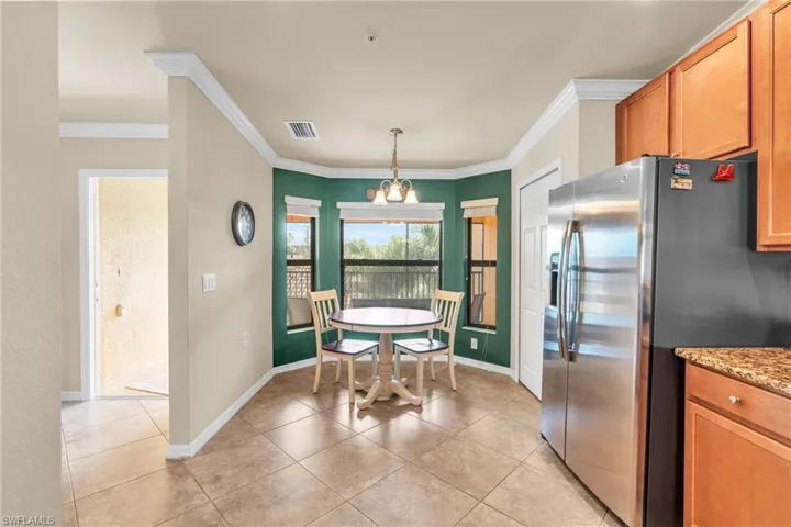 Kitchen with light stone counters, pendant lighting, crown molding, stainless steel fridge with ice dispenser, and light tile patterned floors