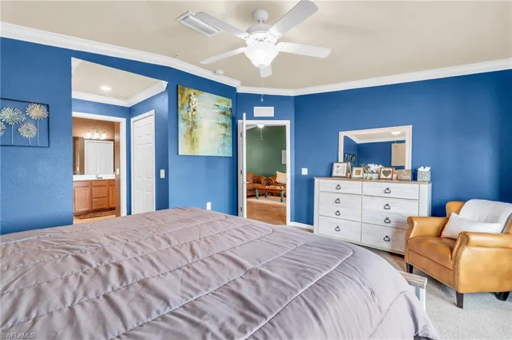 Carpeted bedroom with ornamental molding, ceiling fan, ensuite bath, and a closet