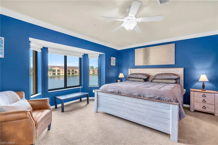 Carpeted bedroom featuring a water view, ornamental molding, and ceiling fan
