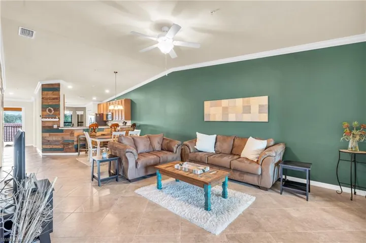 Tiled living room with ceiling fan, crown molding, and vaulted ceiling