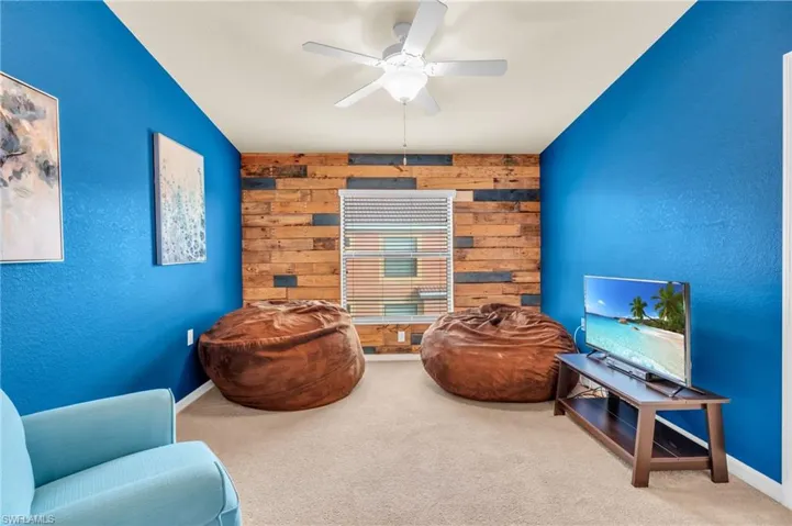 Den with ceiling fan, wood walls, and carpet