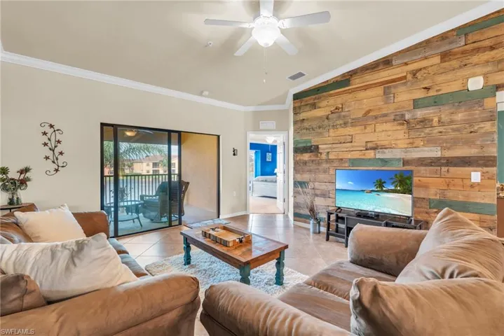 Tiled living room featuring ornamental molding, lofted ceiling, wooden walls, and ceiling fan