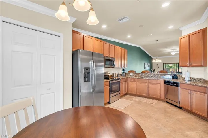 Kitchen with light stone countertops, ornamental molding, pendant lighting, kitchen peninsula, and appliances with stainless steel finishes