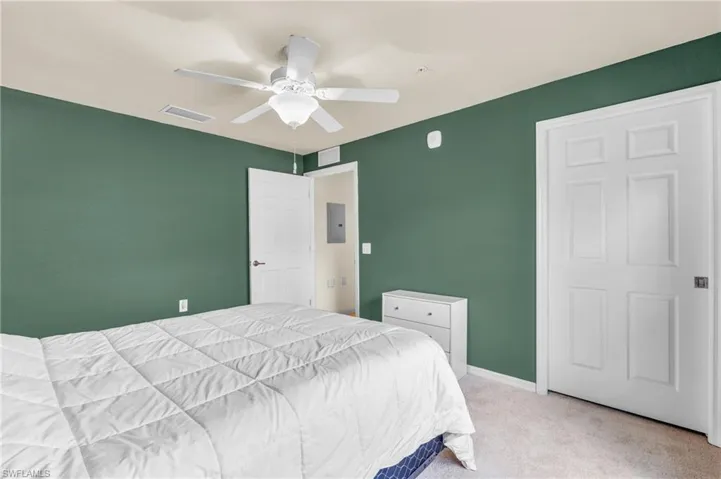 Bedroom with light carpet, ceiling fan, and electric panel