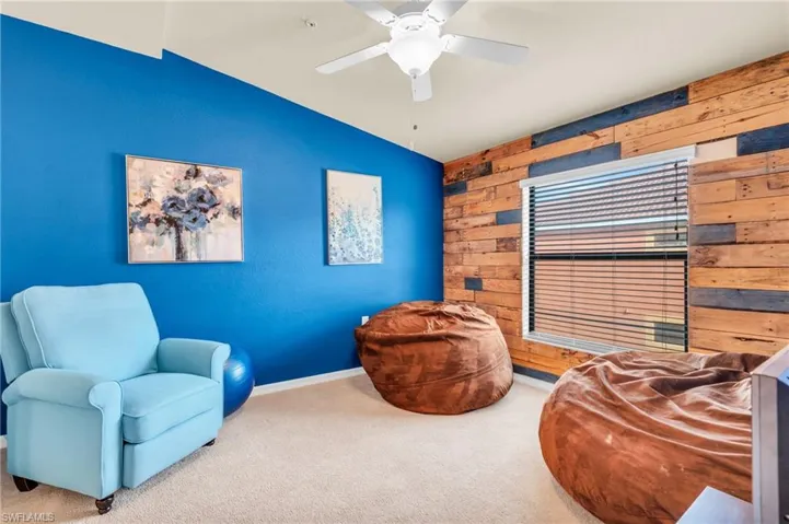 Den area with lofted ceiling, wooden walls, ceiling fan, and carpet