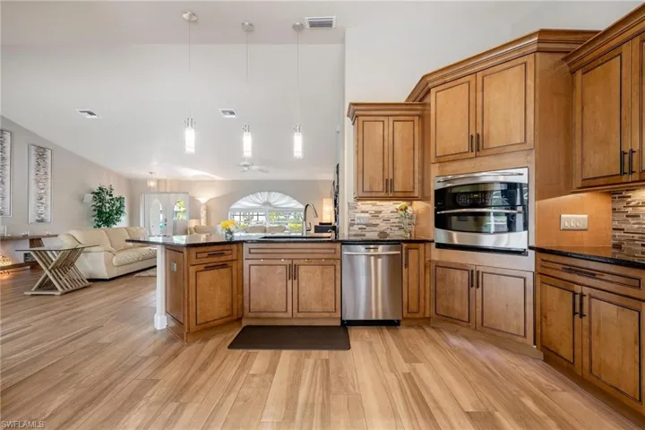 Kitchen with light plank tile flooring, backsplash, stainless steel appliances, pendant lighting, and sink