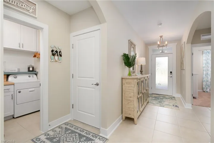 Foyer featuring arched walkways, washer / clothes dryer, light tile patterned floors, and a chandelier