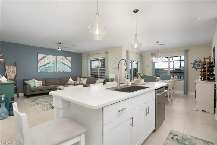 Kitchen with hanging light fixtures, white cabinets, ceiling fan, open floor plan, and a center island with sink