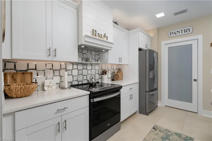 Kitchen featuring range with electric stovetop, stainless steel refrigerator with ice dispenser, white cabinetry, and open shelves