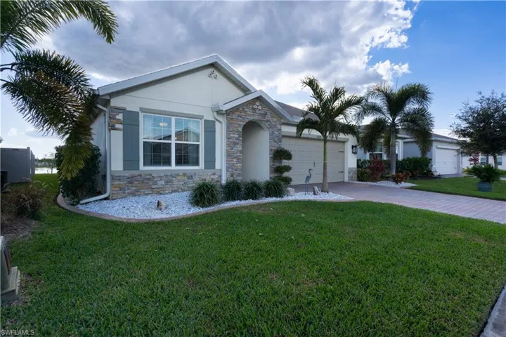 View of front facade featuring stone siding, stucco siding, a front yard, and driveway