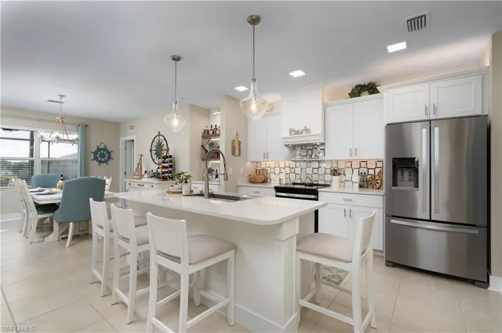Kitchen with appliances with stainless steel finishes, pendant lighting, white cabinetry, and a kitchen bar