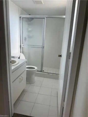 White tiled bathroom featuring a walk-in shower with sliding frosted glass doors, white toilet, and a vanity with a white countertop and base cabinetry