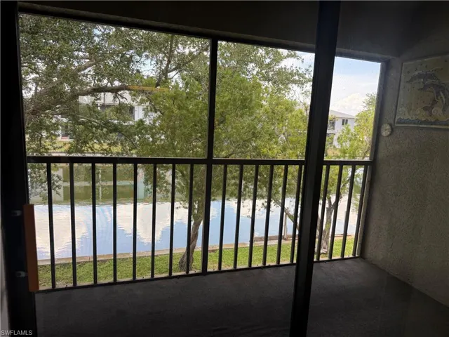 Screened patio overlooking a tranquil water feature, featuring black metal railings, textured wall finish, and mature trees