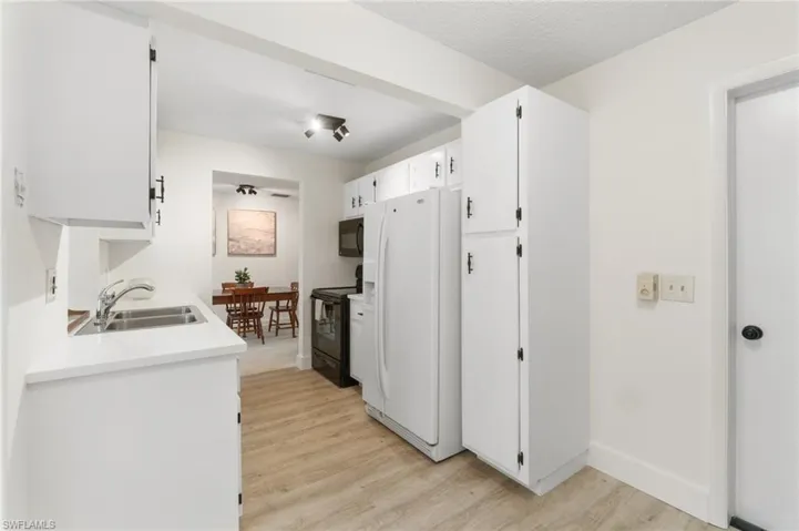 Kitchen with black appliances, white cabinetry, light countertops, light wood-style flooring, and a textured ceiling