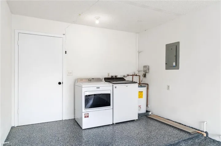 Laundry area with a textured ceiling, electric panel, separate washer and dryer, electric water heater, and light speckled floor