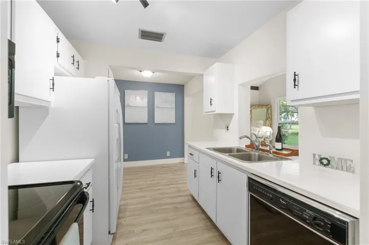 Kitchen with black appliances, light countertops, white cabinets, and light wood finished floors