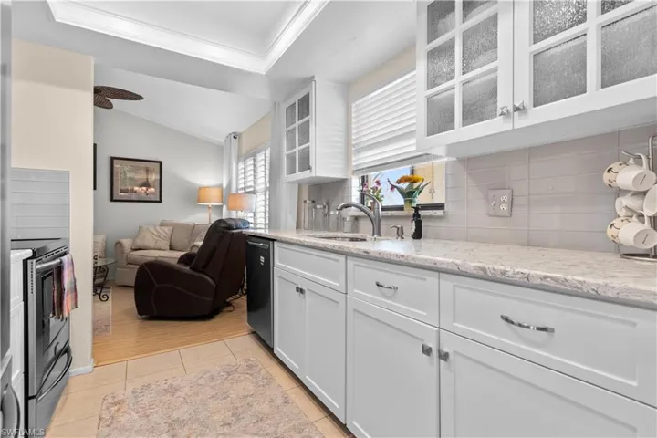 Kitchen with white cabinets, open floor plan, glass insert cabinets, stainless steel electric range, and light stone counters