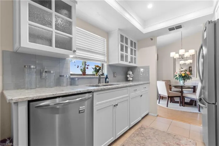 Kitchen featuring glass insert cabinets, white cabinets, stainless steel appliances, and light stone counters