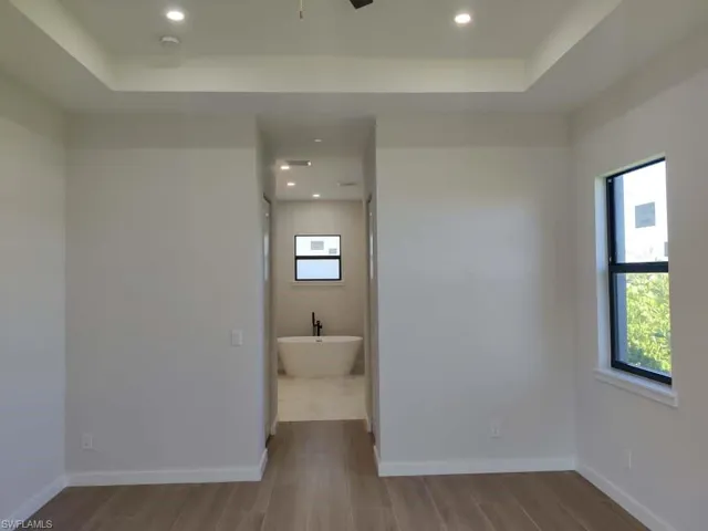 Full bathroom featuring a tray ceiling, a freestanding bath, light wood-type flooring, recessed lighting, and a ceiling fan