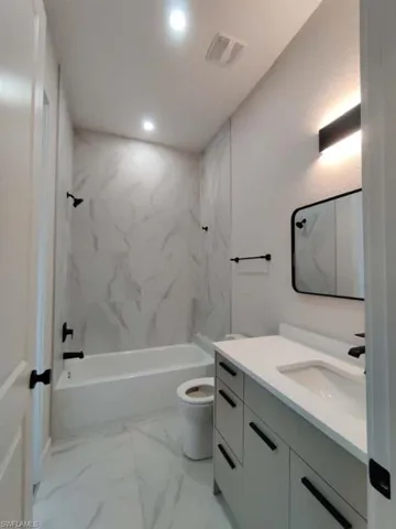 Bathroom with vanity, a combined bath / shower with marble appearance, light marble finish floors, and recessed lighting