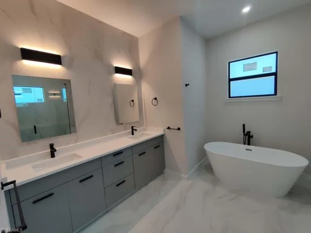 Bathroom with double vanity, a freestanding bath, light marble finish floors, and a marble finish shower