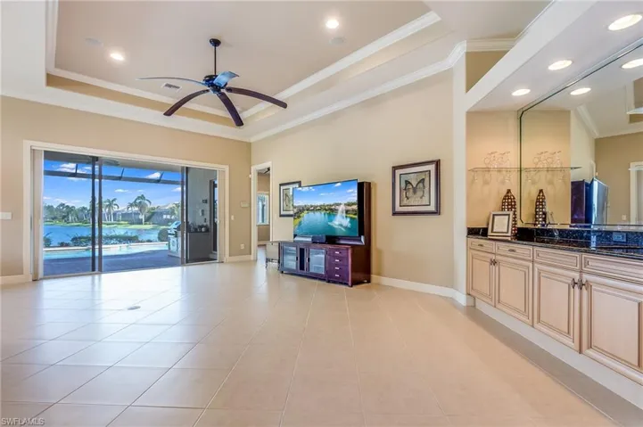 Living room with ceiling fan, a raised ceiling, ornamental molding, and light tile patterned flooring