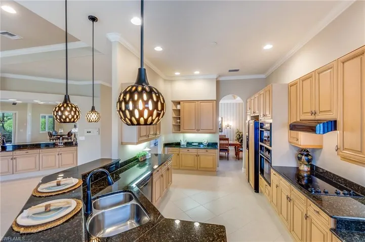 Kitchen featuring light brown cabinetry, sink, black electric cooktop, decorative light fixtures, and crown molding