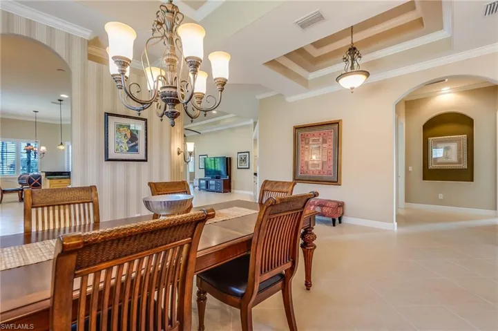 Tiled dining space featuring ornamental molding, an inviting chandelier, and a raised ceiling