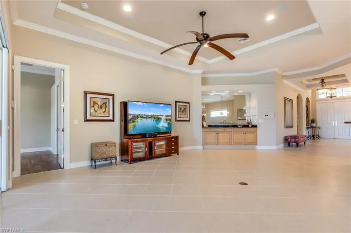 Living room featuring ceiling fan, a raised ceiling, ornamental molding, and light tile patterned floors
