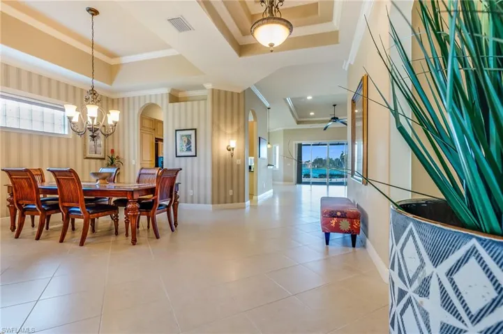 Tiled dining area featuring crown molding, a tray ceiling, and ceiling fan with notable chandelier