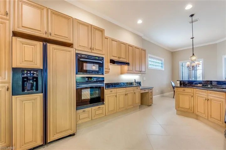Kitchen featuring hanging light fixtures, paneled refrigerator, crown molding, an inviting chandelier, and light brown cabinets