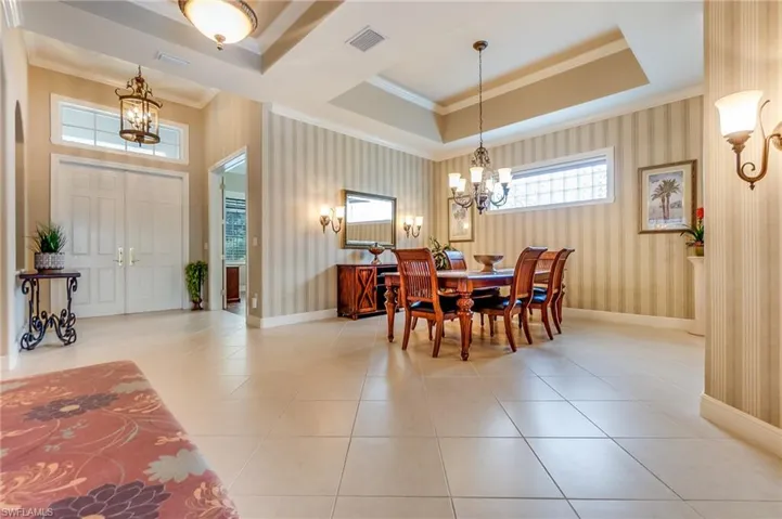 Tiled dining area featuring ornamental molding, a notable chandelier, and a raised ceiling