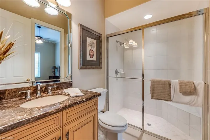 Bathroom with toilet, walk in shower, vanity, and ceiling fan