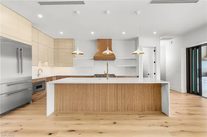 Kitchen with stainless steel appliances, a kitchen island with sink, light wood finish cabinetry, and light stone countertops