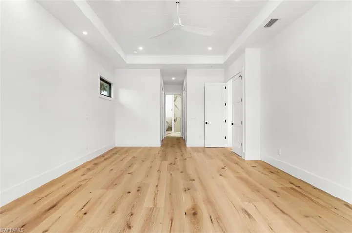 Unfurnished bedroom with recessed lighting, light wood-type flooring, a raised ceiling, ensuite bathroom, and a closet