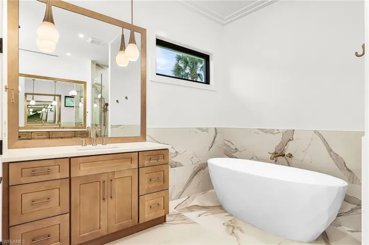 Full bath featuring vanity, light marble finish flooring, wainscoting, and a freestanding bath