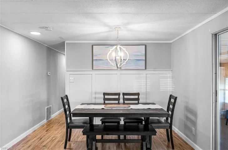 Dining space with a chandelier, wood finished floors, crown molding, a decorative wall, and a textured ceiling