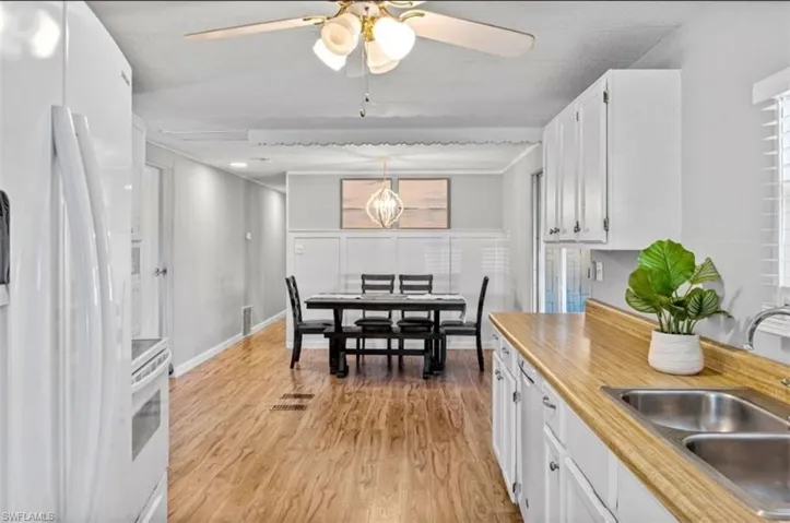 Kitchen featuring white appliances, white cabinets, light countertops, decorative light fixtures, and light wood finished floors