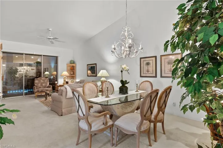 Dining space featuring ceiling fan with notable chandelier, vaulted ceiling, and light carpet