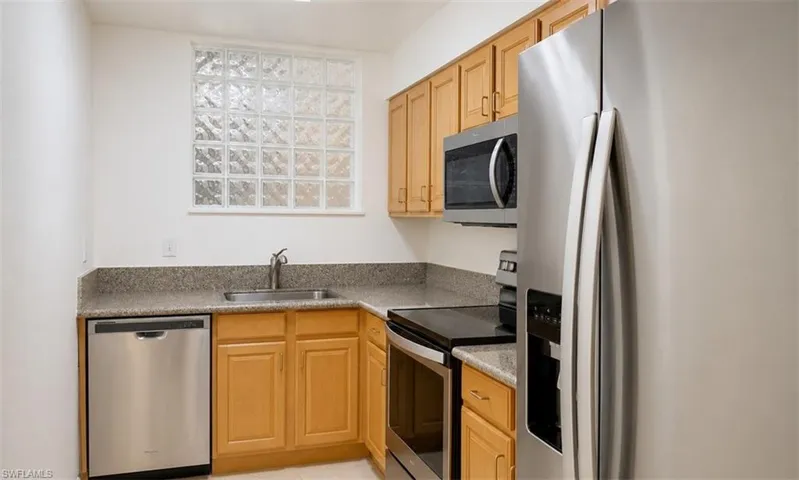 Kitchen featuring light wood cabinetry, stainless steel appliances, a glass block window, and a light-toned countertop