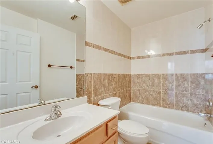 Bathroom featuring a light wood-finish vanity with an integrated sink, a full-width mirror, and a tiled shower-tub combination