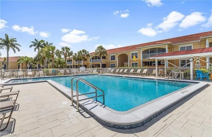 Community swimming pool with a mosaic tile border and integrated steps, surrounded by light-toned paver decking