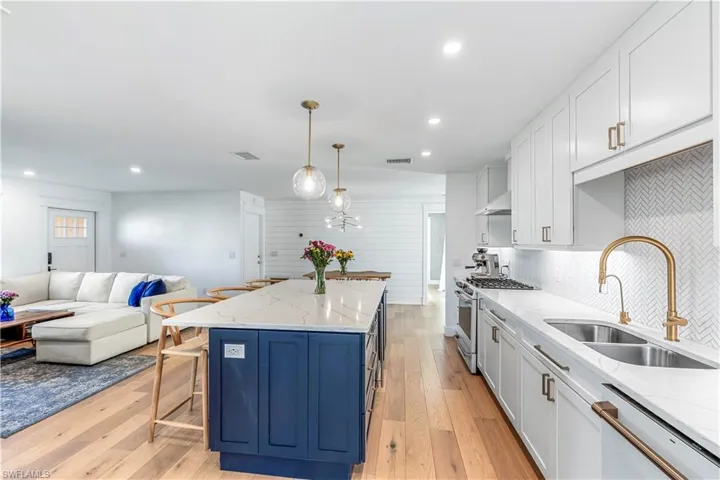 Chic Kitchen featuring large center island light wood-type flooring, white cabinets, stainless steel Cafe' appliances, and decorative light fixtures.