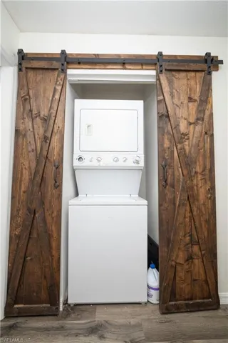 Wood-finish flooring with a laundry closet featuring a stacked washer and dryer