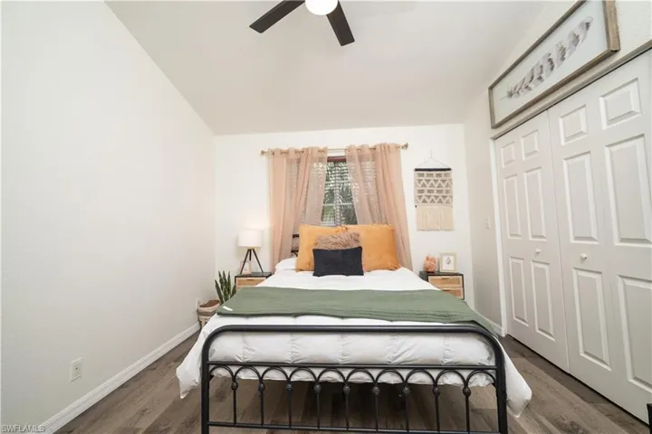 Vaulted ceiling with a ceiling fan, wood-finish flooring, window with natural light, and bi-fold closet doors